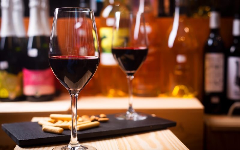 Glass of red wine prepared for tasting in a winery. Bottles on background